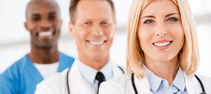Medical doctors team. Medical doctors team. Confident female doctor looking at camera and smiling while her colleagues standing in a row behind her